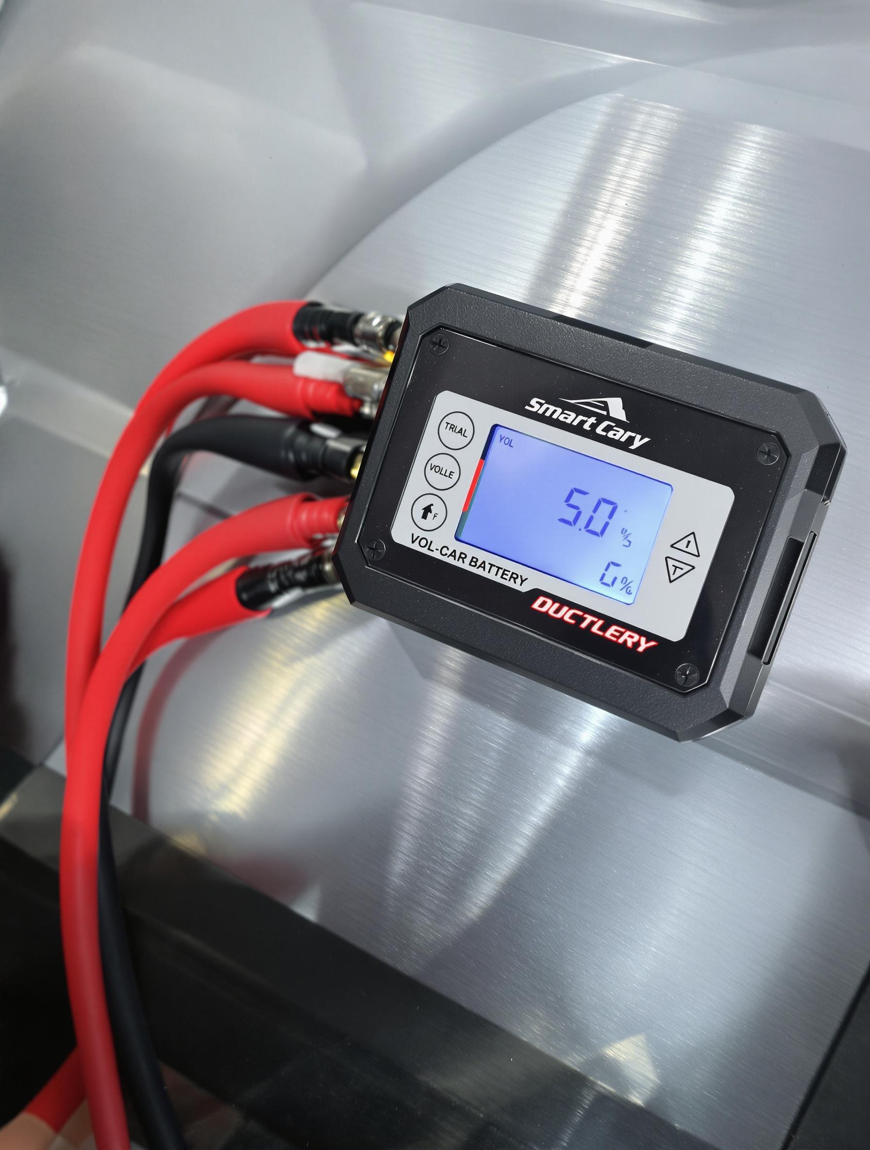 Chargeur intelligent branché sur une batterie de voiture avec câbles isolés et écran numérique indiquant le voltage.